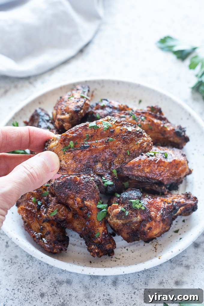 Air Fryer Wings: Crispy Perfection 8 A hand reaching for a crispy air fryer chicken wing from a plate full of wings
