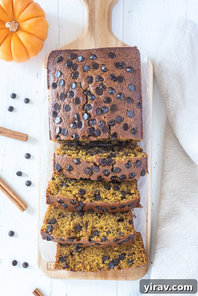 A freshly baked loaf of gluten-free pumpkin bread, half-sliced to reveal its inviting texture, sits on a wooden cutting board, ready to be enjoyed.
