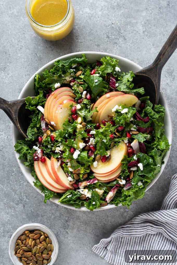 Kale and apple salad in a bowl with salad servers, ready to be enjoyed as a meal.