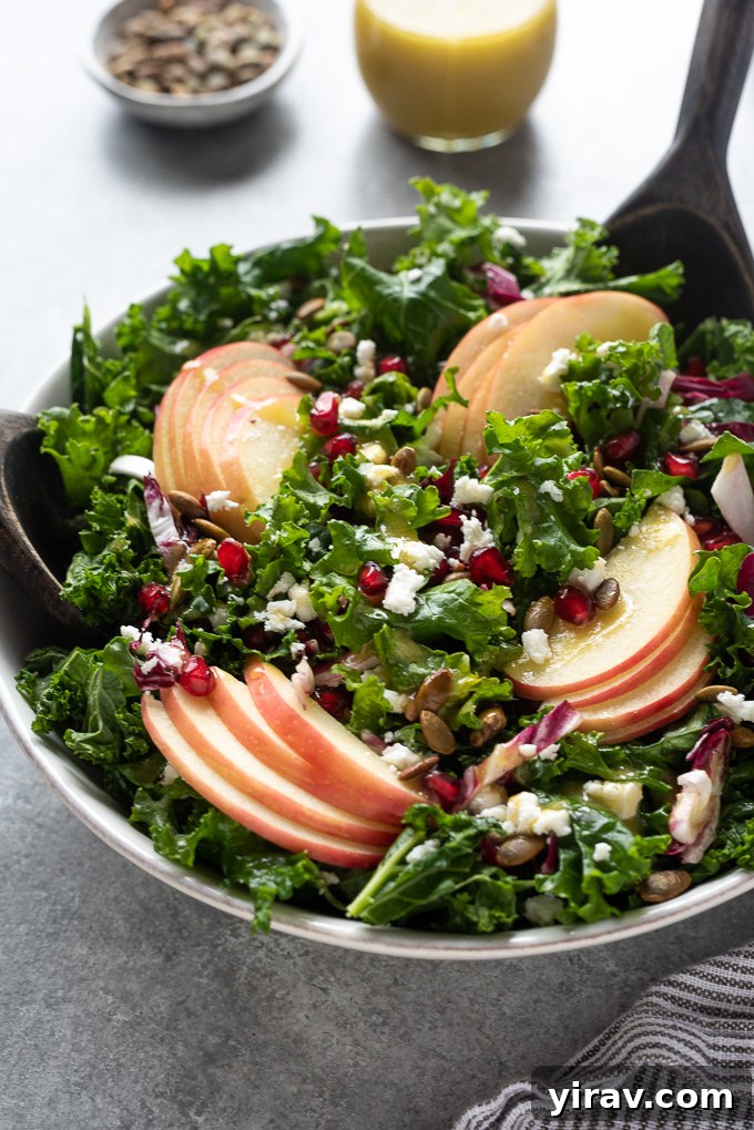 Kale apple salad with salad servers digging into the bowl, ready to serve.