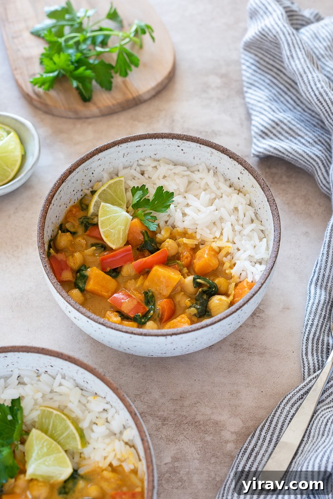 A bowl of chickpea curry served alongside fluffy white rice, fresh lime wedges, and a sprinkle of cilantro. The curry looks rich and inviting.