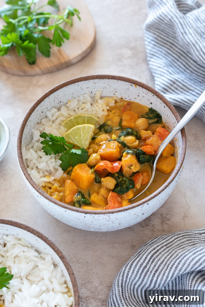 A close-up of a spoon digging into a bowl of Instant Pot Sweet Potato Chickpea Curry, highlighting the rich texture and vibrant ingredients. It's a wholesome, satisfying vegan dinner that's quick, gluten-free, and great for meal prep.