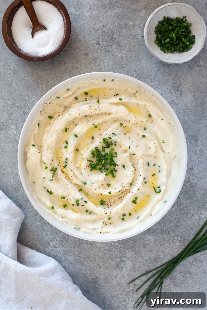 Creamy Garlic Mashed Cauliflower 3 A pristine white serving bowl filled with creamy garlic mashed cauliflower, garnished generously with fresh green chives, highlighting its inviting texture.