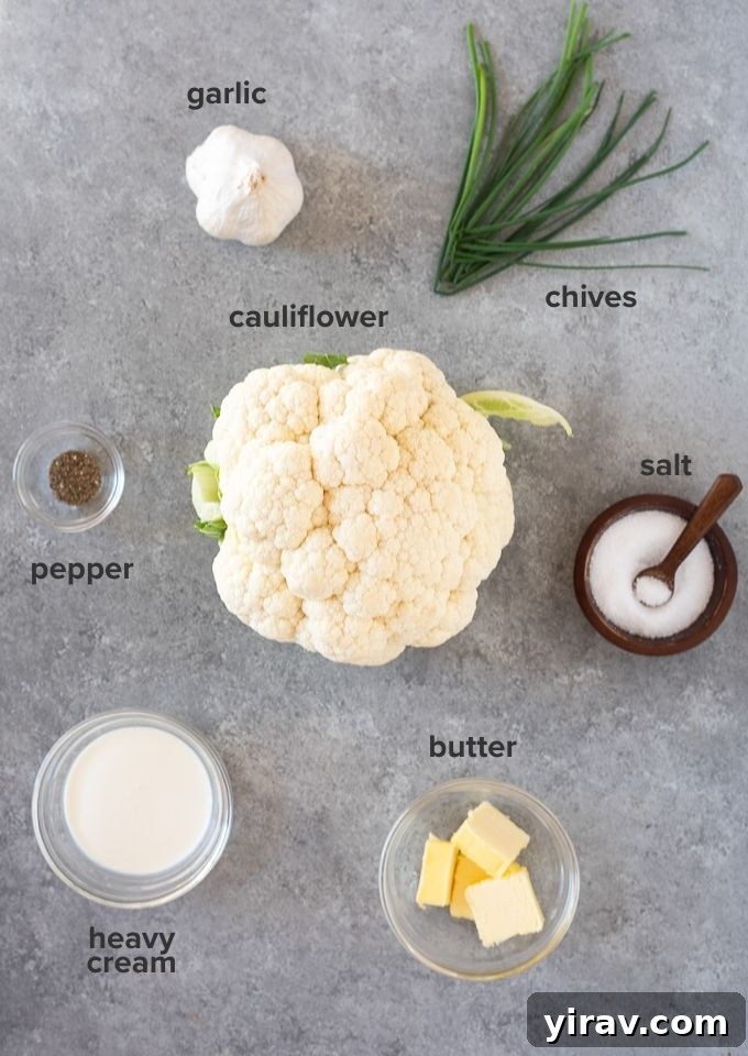 Creamy Garlic Mashed Cauliflower 4 Individual ingredients for garlic mashed cauliflower including a head of cauliflower, garlic cloves, a stick of butter, heavy cream, and a bunch of chives.