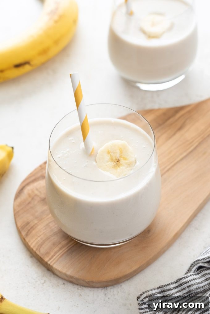 Quick Banana Bliss Smoothie 2 Creamy Banana smoothie in a glass with a straw and a fresh banana slice garnish, set against a bright background.