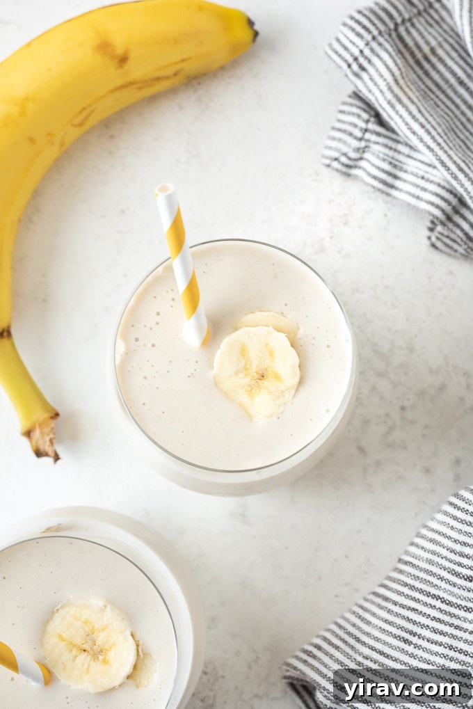 Quick Banana Bliss Smoothie 3 Close-up of a refreshing banana smoothie with a straw and a banana slice, highlighting its creamy texture.
