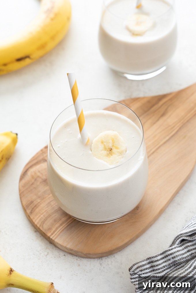 Quick Banana Bliss Smoothie 6 A glass of banana smoothie sitting on a small wooden cutting board, garnished with a banana slice.