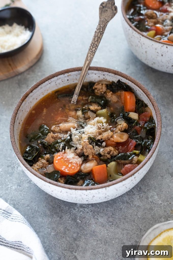 A steaming bowl of vibrant Italian sausage kale soup with a spoon digging in, garnished with fresh parmesan cheese.