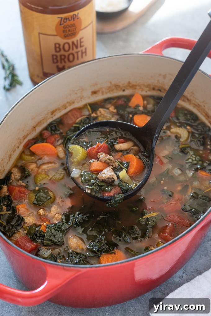 A ladle scooping steaming Italian sausage and kale soup from a Dutch oven, highlighting the rich texture and ingredients.