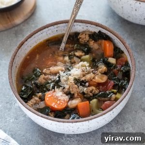 Italian sausage kale soup in a white bowl with spoon digging in