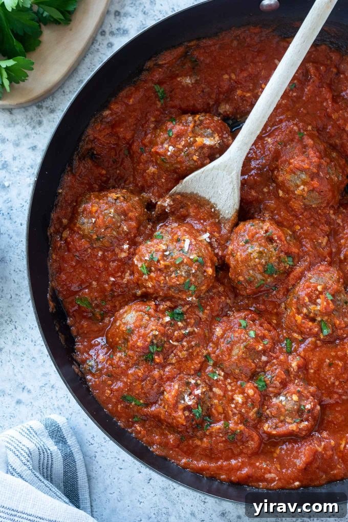 Simple Oven Roasted Meatballs 2 Oven baked meatballs simmering in a rich tomato sauce within a cast-iron skillet, garnished with fresh parsley.
