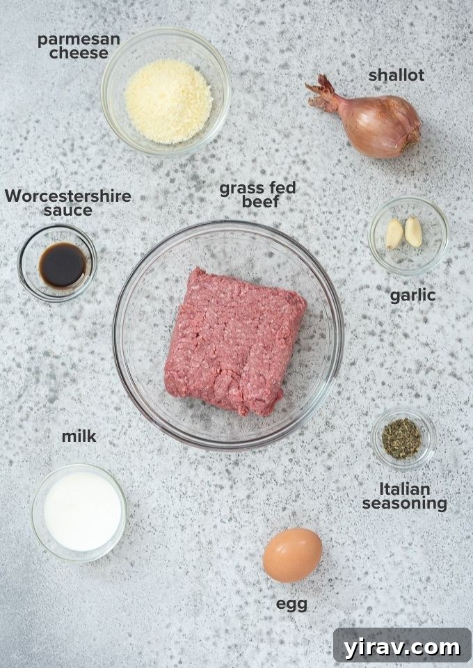 Simple Oven Roasted Meatballs 4 A collection of ingredients for baked meatballs laid out on a white surface, including ground beef, a shallot, parmesan cheese, and various spices.