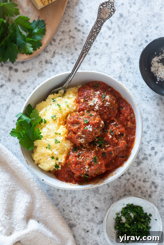 Simple Oven Roasted Meatballs 8 A bowl filled with gluten-free baked meatballs served alongside a portion of polenta, garnished with herbs.