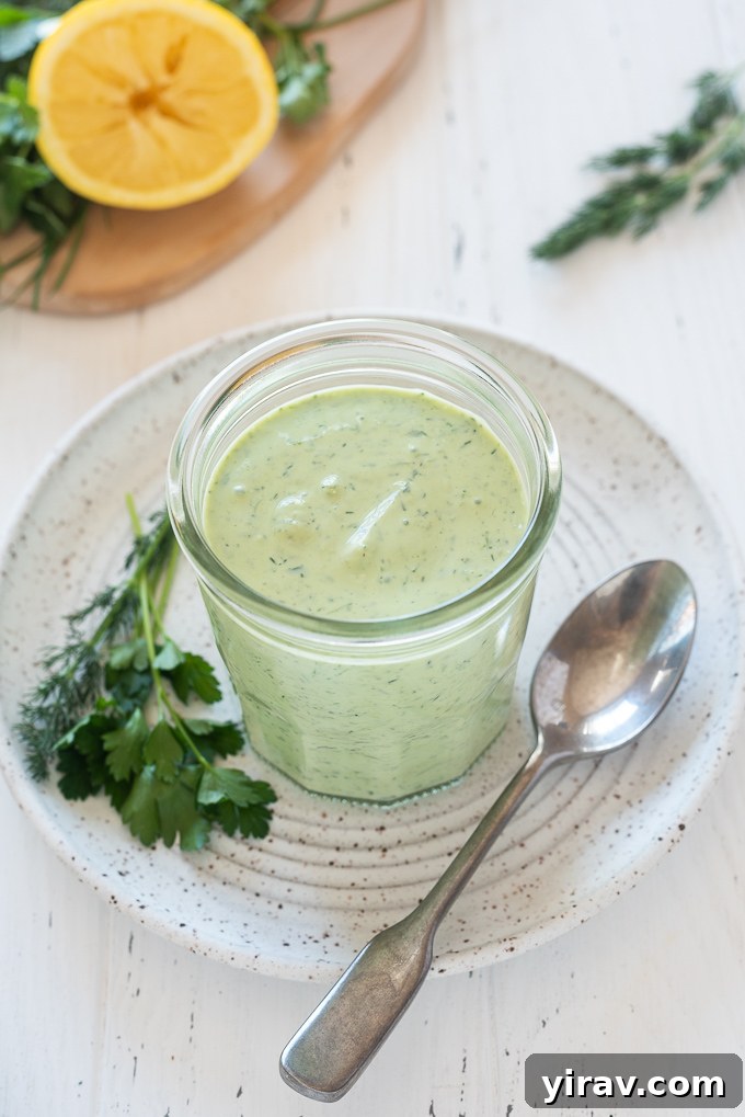 The Perfect Green Goddess Dressing 3 Green Goddess dressing in a jar surrounded by fresh herbs and a spoon, emphasizing its natural ingredients.