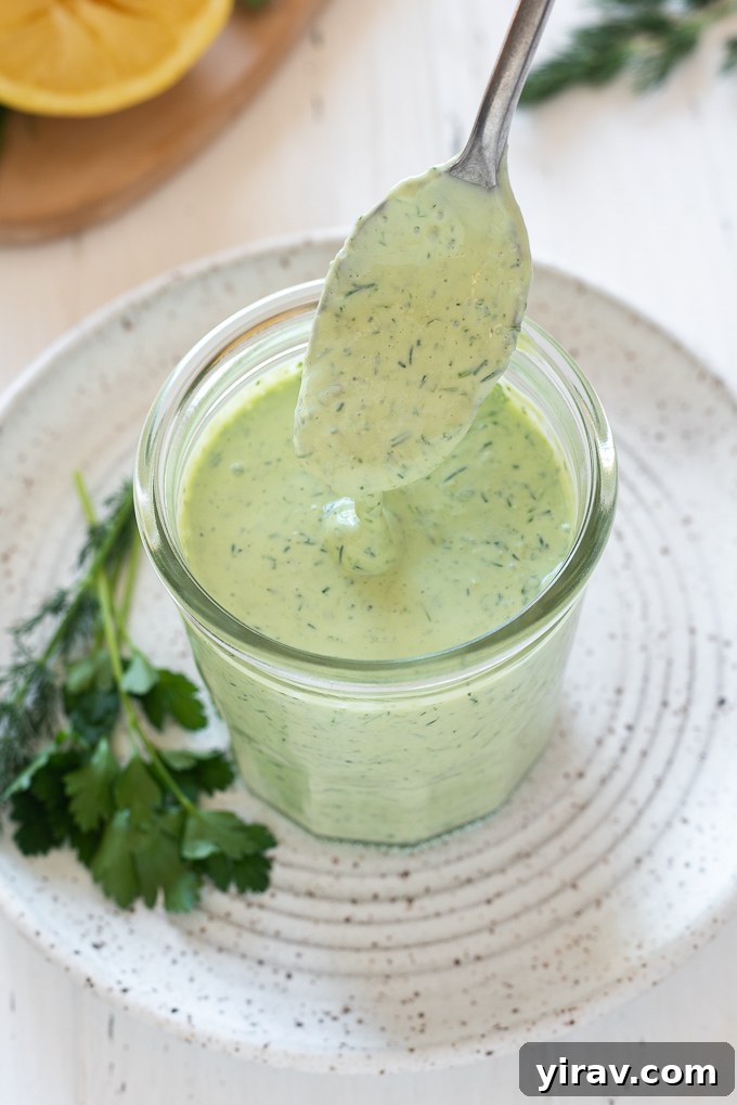 The Perfect Green Goddess Dressing 7 Green Goddess dressing being drizzled from a spoon into a jar, showcasing its smooth consistency.