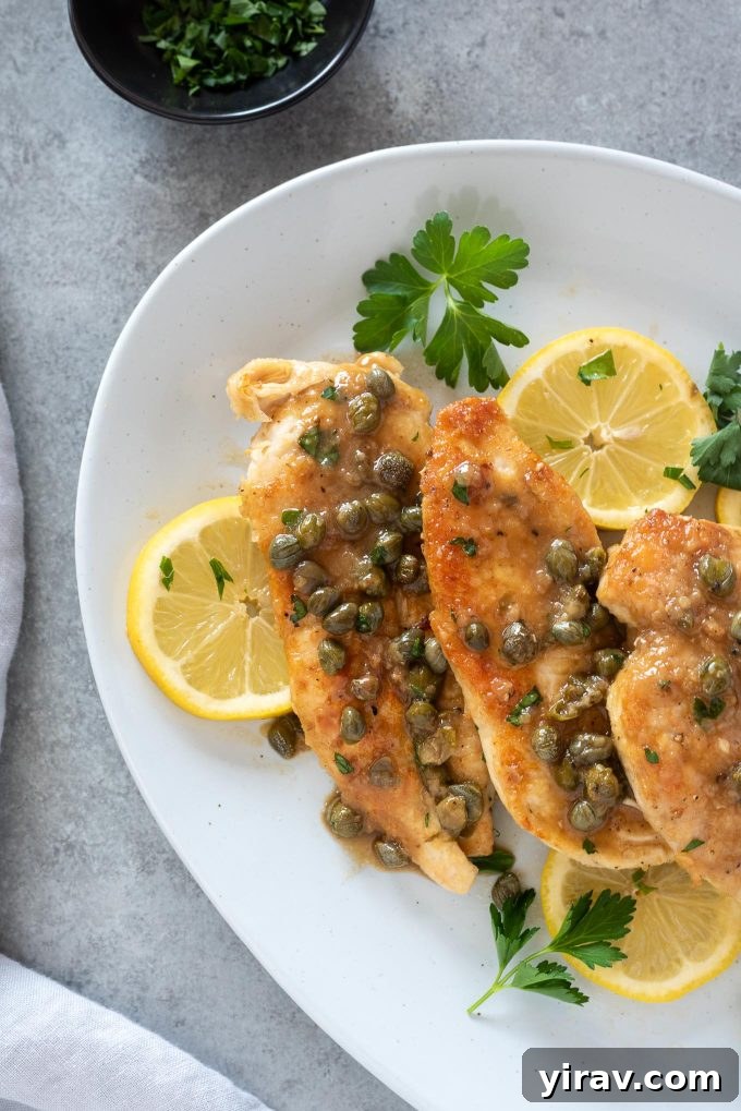 Deliciously Simple Chicken Piccata 2 Chicken piccata on a serving plate, garnished with fresh parsley and lemon slices.