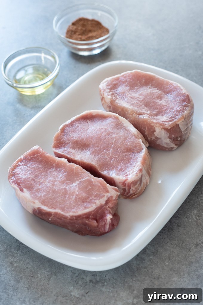 A flat lay image displaying the simple ingredients required for air fryer pork chops: boneless pork chops, a bottle of high-heat oil, and a small bowl of mixed spices.
