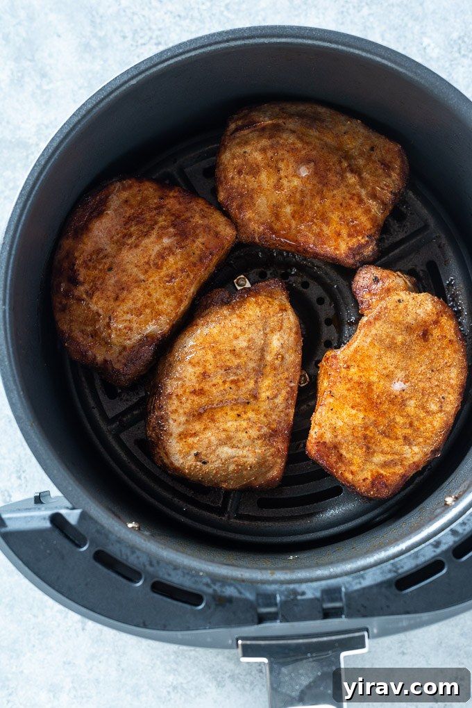 Two boneless pork chops cooking in an air fryer basket, showing their golden-brown and crispy texture as they cook.