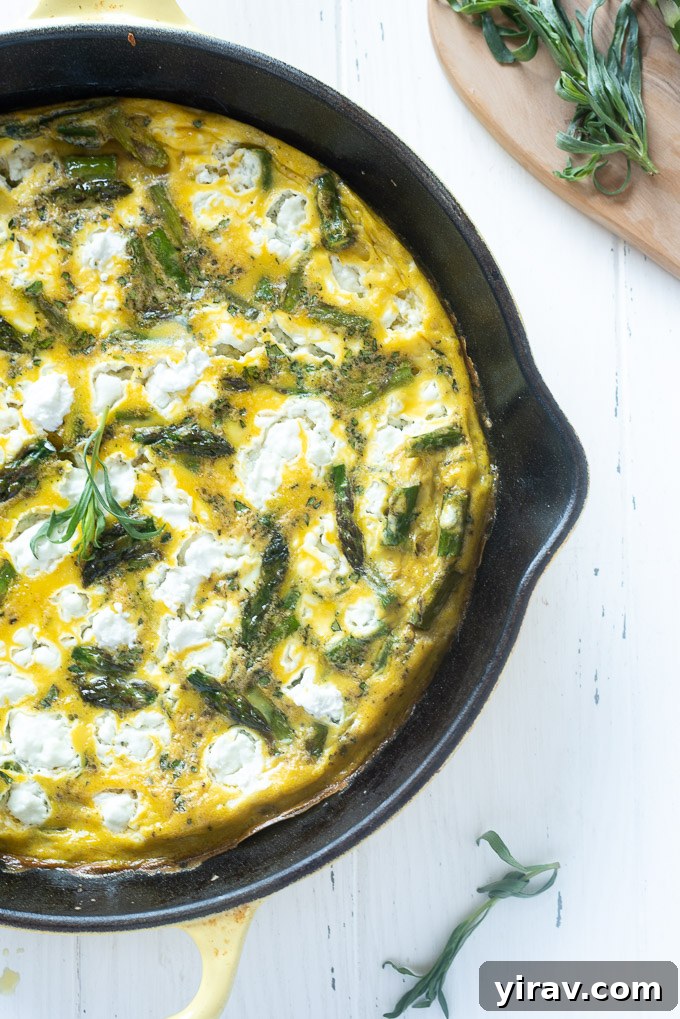 Close-up of a golden Asparagus Frittata with crumbled goat cheese and fresh tarragon leaves, still in the skillet.