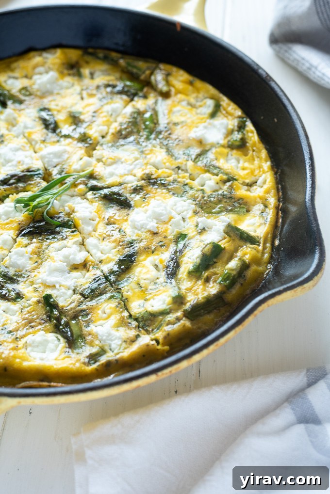 A perfectly sliced Asparagus Frittata with Goat Cheese in a cast iron skillet, showcasing its fluffy texture and vibrant ingredients.