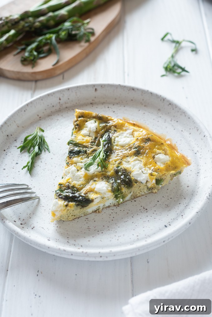 A single slice of Asparagus Frittata with Goat Cheese on a plate, garnished with a sprig of fresh tarragon.