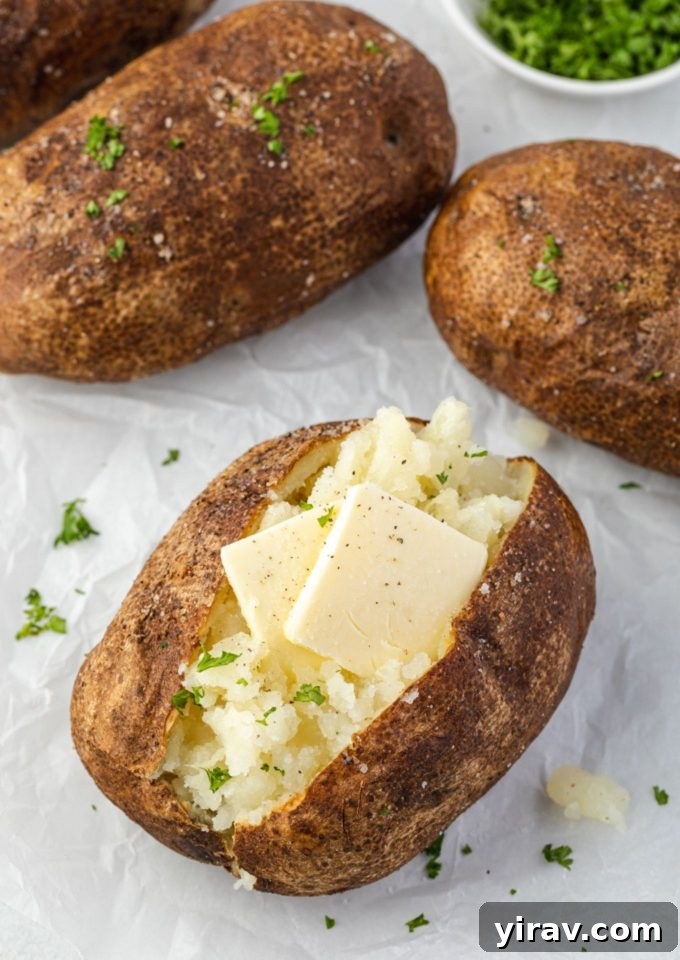 Air fryer baked potatoes with pats of butter and parsley, showcasing crispy skins and fluffy interior