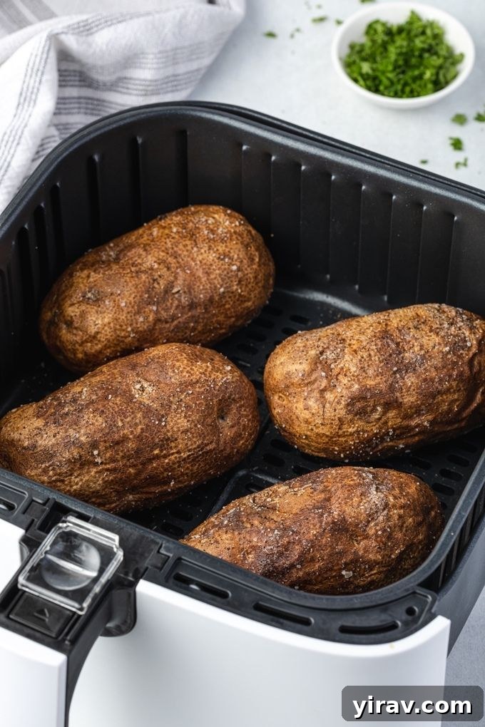 Cooked baked potatoes resting in an air fryer basket, perfectly golden brown and crispy