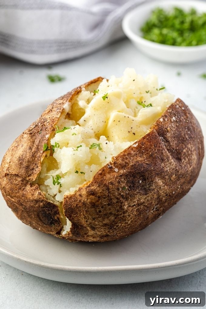 Close-up of an air fryer baked potato on a plate, split open with melted butter inside