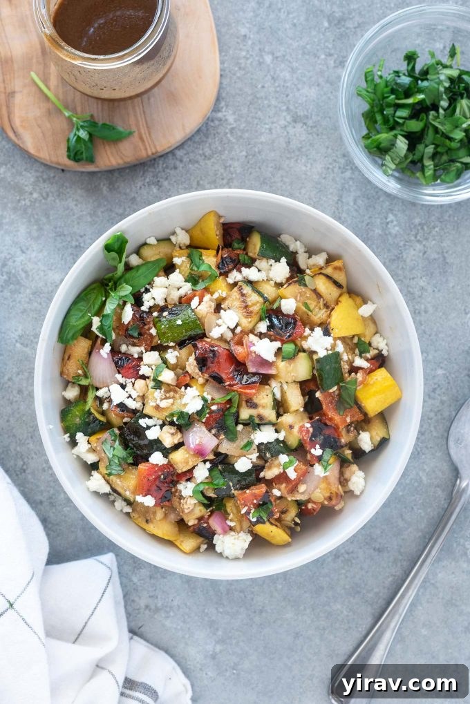 A colorful bowl of grilled vegetable salad with feta cheese and fresh basil, set on a rustic linen cloth.