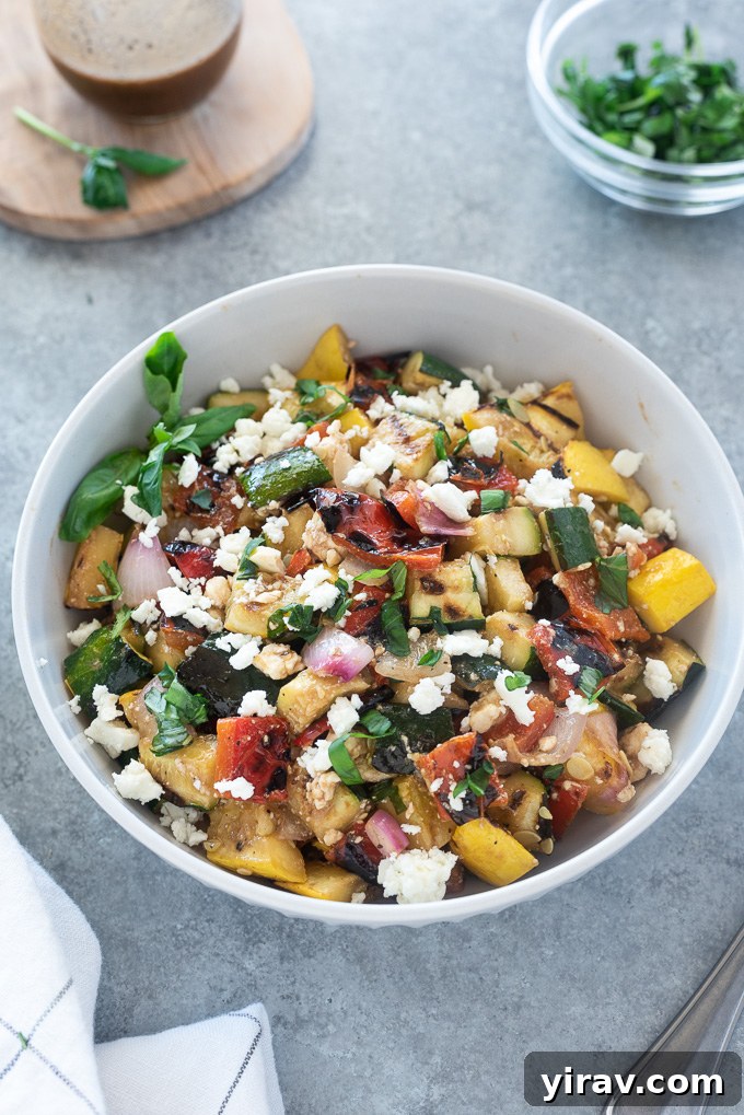 Grilled vegetable salad with crumbled feta cheese in a pristine white serving bowl.