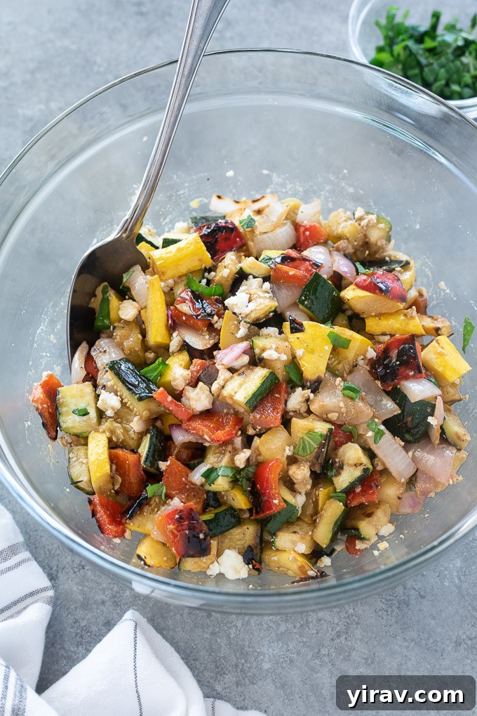 Grilled vegetable salad in a mixing bowl, ready to be served, with a wooden serving spoon.