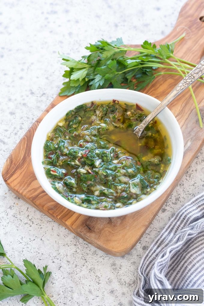 Freshly made Chimichurri sauce in a glass bowl with a spoon, ready to be served.