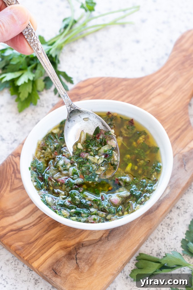 A spoon lifting a generous portion of green chimichurri sauce from a bowl, highlighting its vibrant texture.