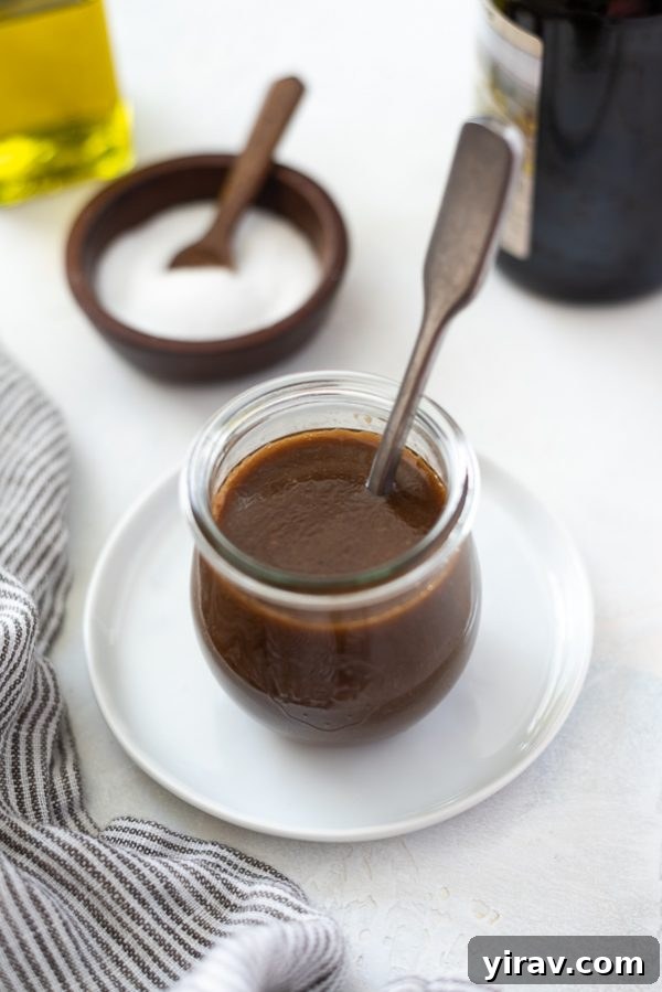 Balsamic vinaigrette dressing in a clear jar with a spoon, highlighting its rich, dark color and inviting texture.