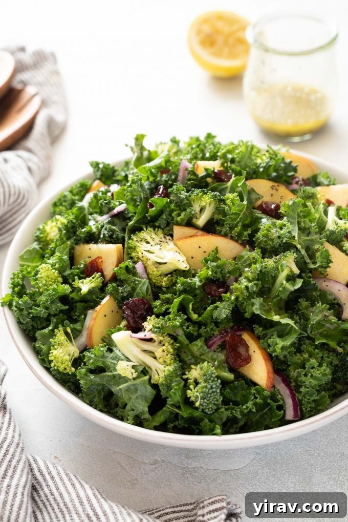Broccoli kale salad in a white bowl with lemon poppy seed dressing nearby, showcasing a fresh and healthy meal.