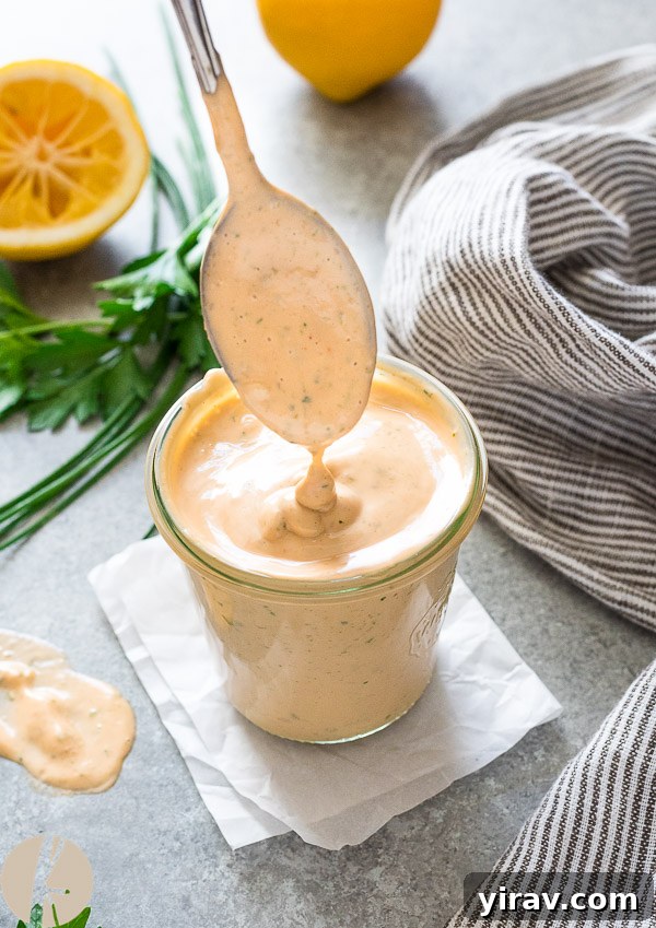 Creamy Louie salad dressing drizzling from a spoon into a jar, showcasing its smooth and inviting texture.