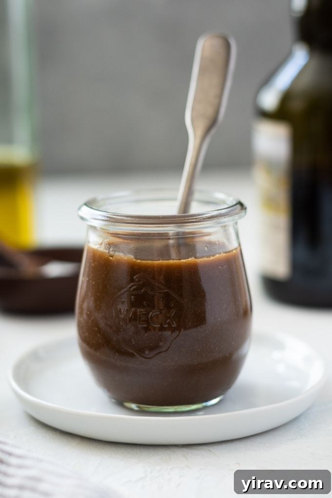 A jar of rich balsamic vinaigrette dressing with a wooden spoon inside, set against a rustic background, highlighting the homemade freshness.