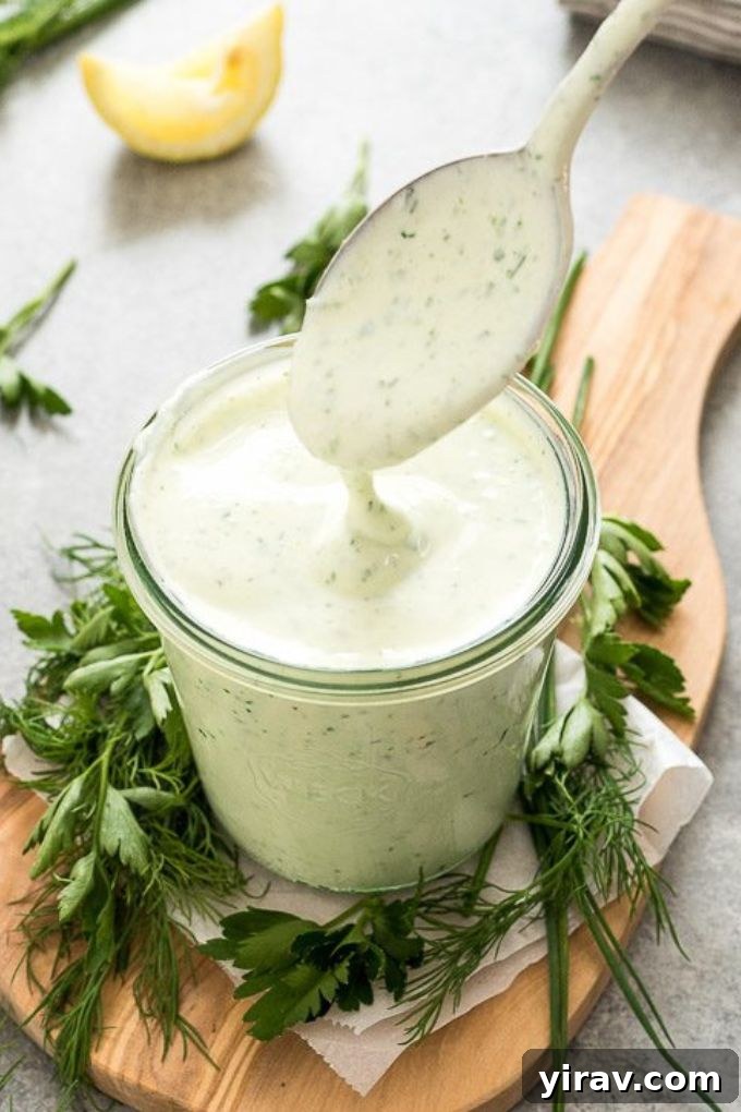 A spoon drizzling rich Greek yogurt ranch dressing into a clear glass jar, emphasizing its creamy texture and homemade appeal.