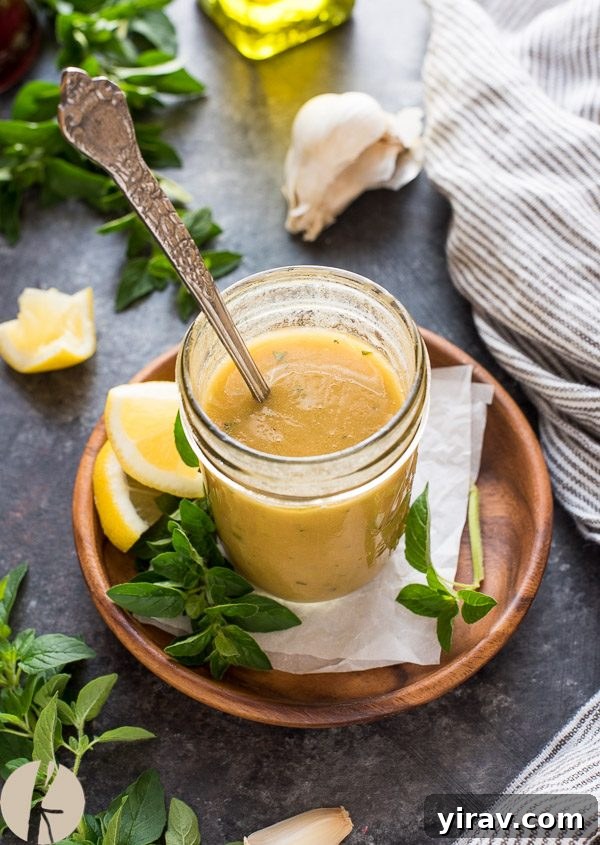 Authentic Greek salad dressing in a jar with a spoon, showcasing its rich herb and olive oil blend.