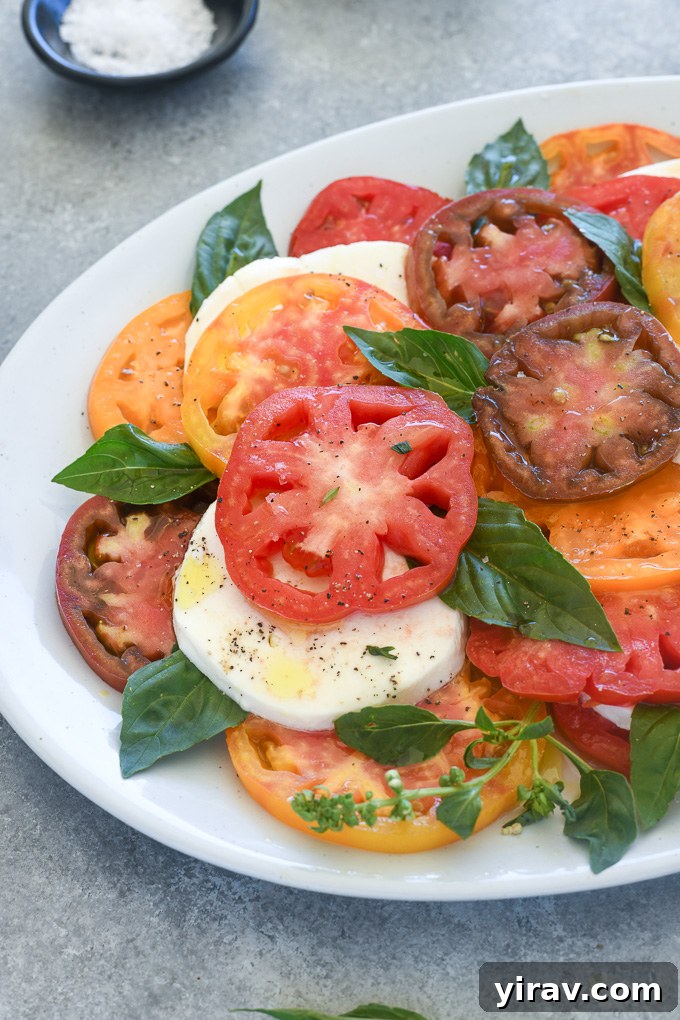 Simple Caprese Perfection 3 Tomato mozzarella salad layered on a white platter with fresh basil leaves tucked in