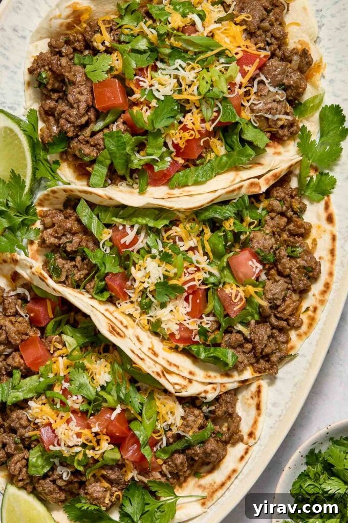 Delicious ground beef tacos artfully arranged on a serving platter, accompanied by vibrant lime wedges and fresh cilantro sprigs.