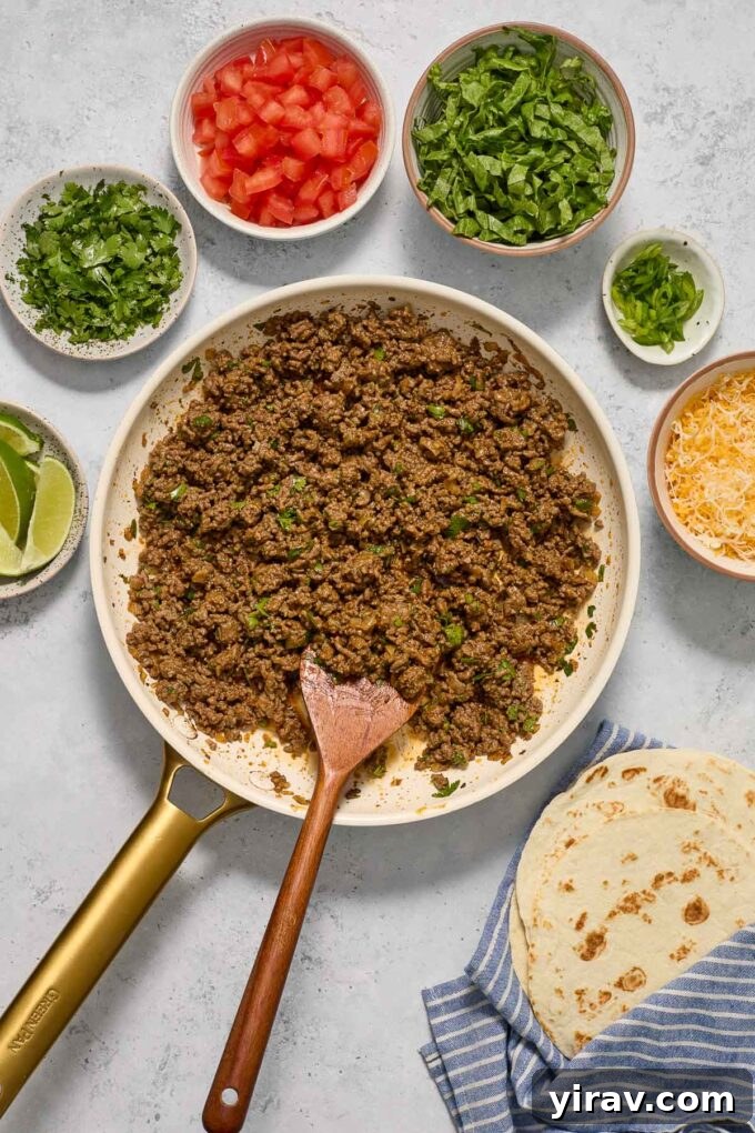 Richly seasoned ground beef taco filling in a cast iron skillet, surrounded by a colourful array of fresh taco toppings.