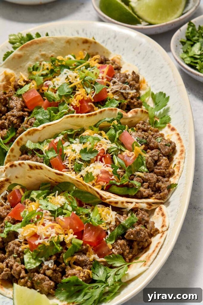 Two beautifully garnished ground beef tacos on a wooden board, with fresh cilantro and lime wedges providing a vibrant contrast.