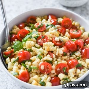 Spoon buried in a bowl of corn and tomato salad