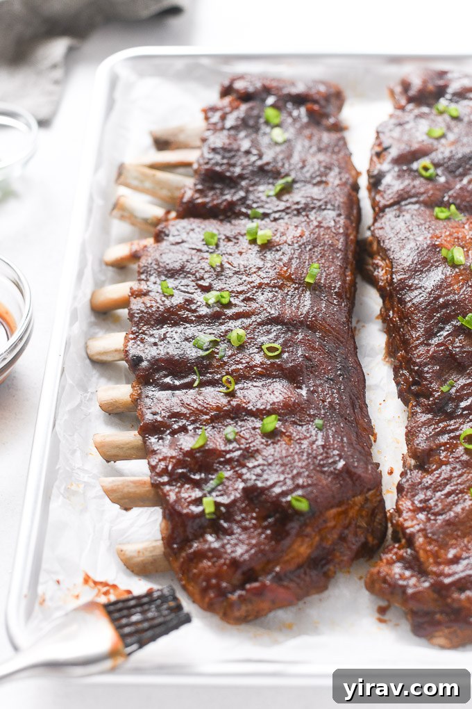 Two racks of Instant Pot pork ribs on a baking sheet, ready for broiling with BBQ sauce.