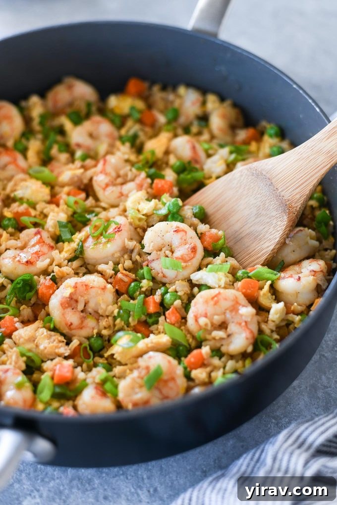 Wooden spoon digging into pan of shrimp fried rice, showcasing juicy shrimp and vibrant vegetables