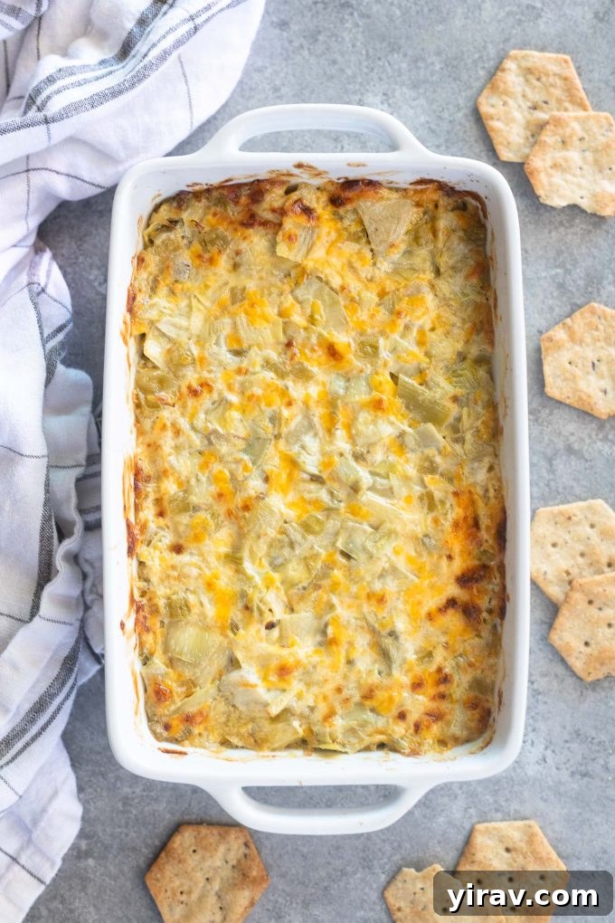 Irresistible Hot Artichoke Dip 2 Golden brown hot artichoke dip in a baking dish, surrounded by crispy crackers, ready to be served at a party.