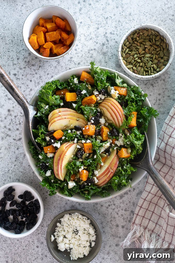 A large bowl of Fall Harvest Salad with salad servers digging in, showcasing the rich textures and colors of kale, roasted squash, apple, and feta, indicating it's ready to be enjoyed.