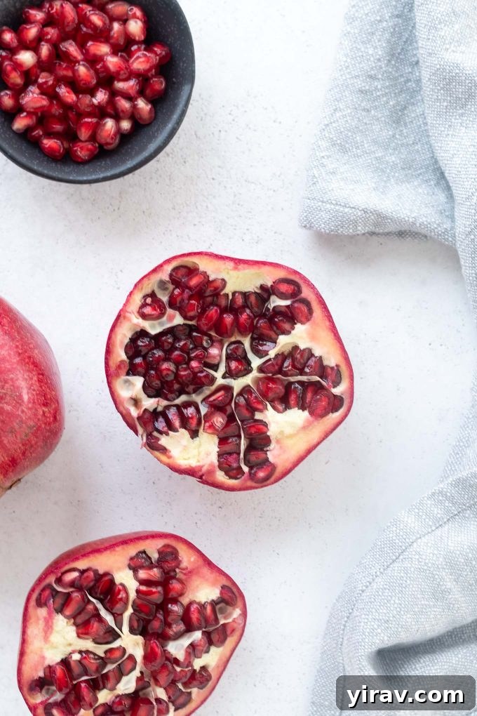 A halved pomegranate next to a bowl brimming with bright red pomegranate arils, highlighting the fruit's edible seeds.