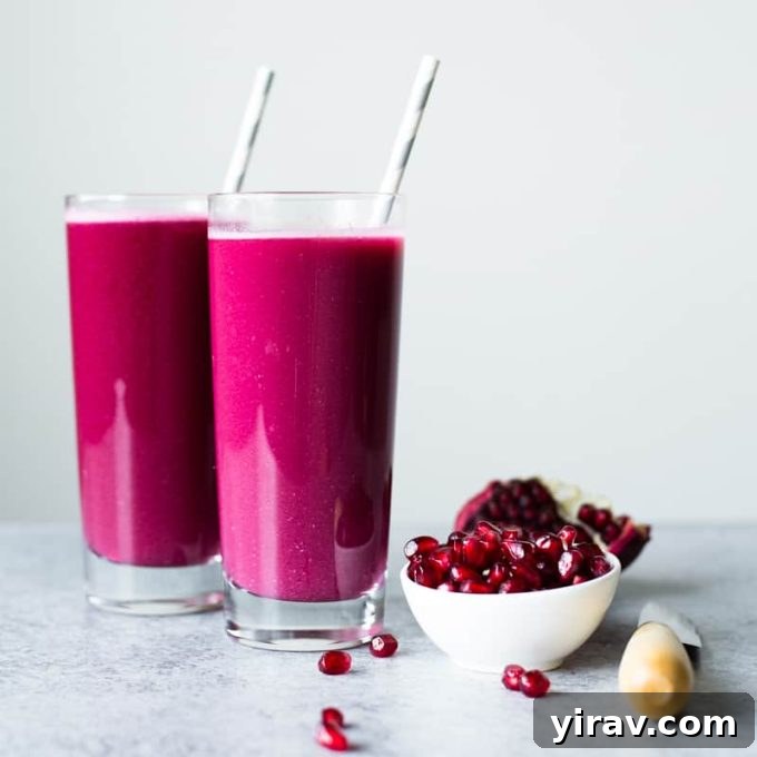 A glass of freshly made Pomegranate Juice with a sliced pomegranate and arils in the background.